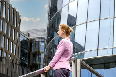 Low angle view of woman standing on railing against buildings