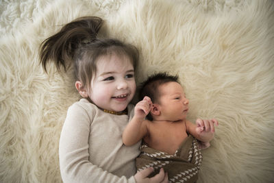 Big sister hugs newborn brother while laying on fuzzy rug