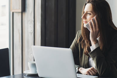 Businesswoman using smart phone looking away in cafe