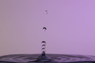 Close-up of drop falling on water against gray background