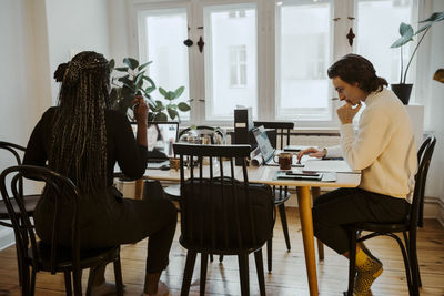 Businesswoman attending video call while male entrepreneur using laptop sitting at desk in home office