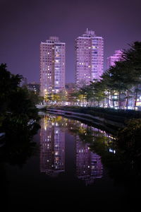 Illuminated buildings by lake against sky in city at night