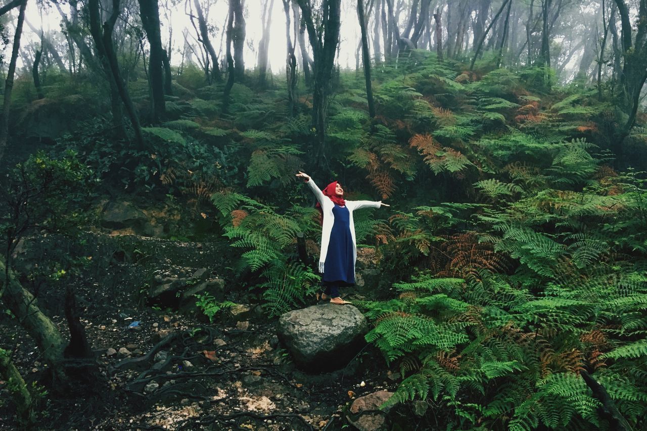 WOMAN STANDING BY TREE IN FOREST