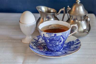Hot tea and a soft boiled egg for breakfast on a table with a blue background on white linen.