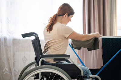 Side view of young woman holding wheelchair in gym