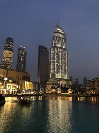 Illuminated buildings by river against sky at night