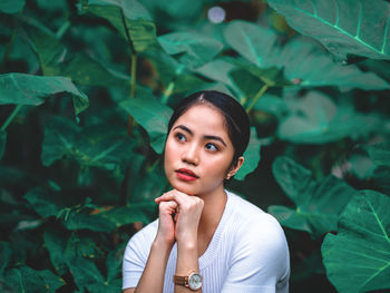 Young woman looking away while standing by plant outdoors