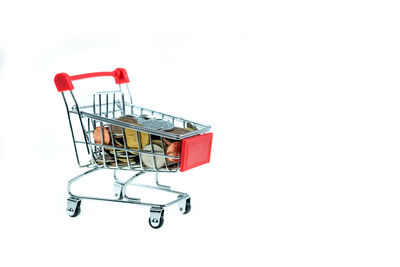 Close-up of coins and shopping cart over white background