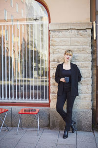 Full length portrait of confident businesswoman holding coffee cup outside office