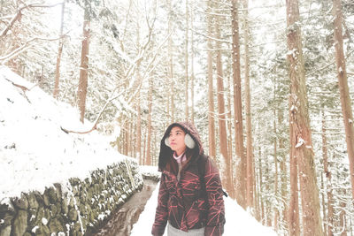 Woman standing amidst trees in forest during winter