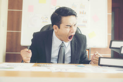 Cheerful businessman clenching fist while sitting on table at office