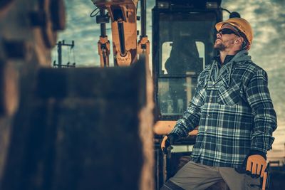 Man wearing sunglasses standing by earth mover at construction site
