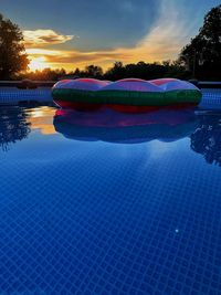 Swimming pool by lake against sky during sunset