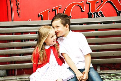 Happy girl sitting on bench against red wall