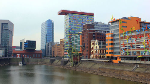 Buildings by river against sky in city