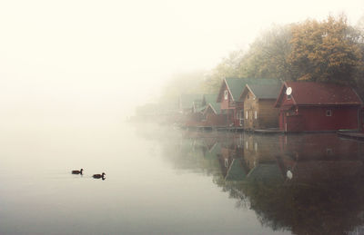 People in lake against sky during foggy weather