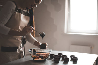 Midsection of female chef preparing cooking cup cake at kitchen