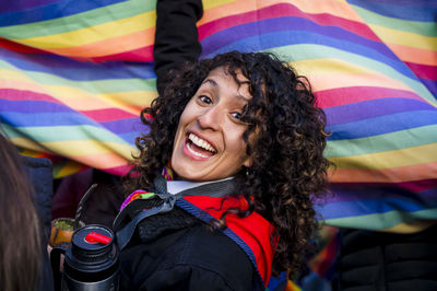 Woman looking at camera while holding a rainbow flag in an lgbtq pride march.