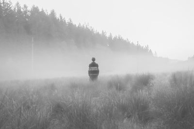 Rear view of man on field against sky during foggy weather