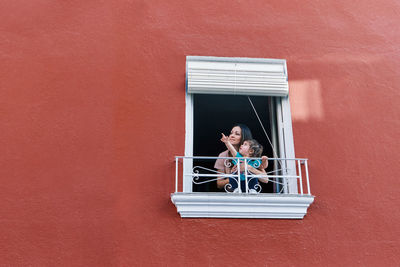 Woman clapping in the window of her house with her daughter on a red background