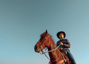 Low angle view of young man looking away while siting on horse against clear sky