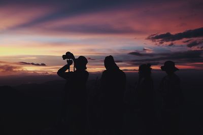 Silhouette people photographing sea against sky during sunset