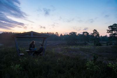 Men sitting on field against sky during sunset