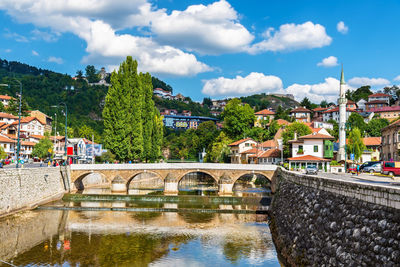 Bridge over river by buildings against sky in city