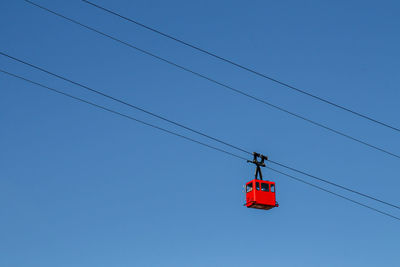 Low angle view of overhead cable cars against clear blue sky