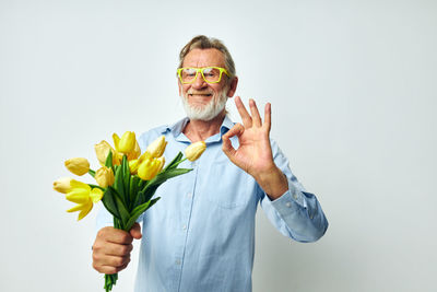 Portrait of young man holding flowers against white background
