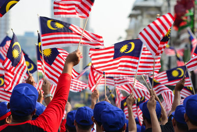 Rear view of people waving malaysian flags in city