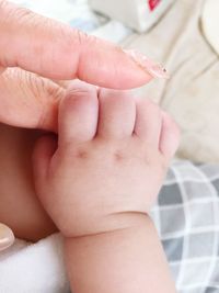 Cropped image of mother holding baby hand on bed