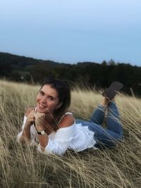 Portrait of young woman smiling while lying on grassy field against clear sky