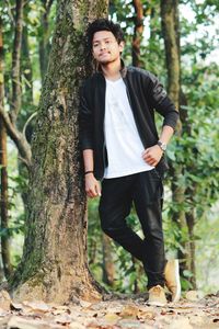 Man standing by tree trunk in forest