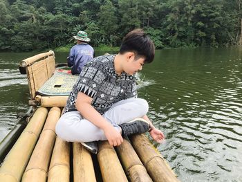 Full length of man sitting on wooden post in lake