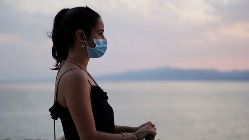 Portrait of woman with mask  against sea at sunset