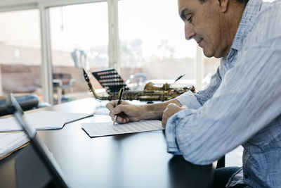 Man writing musical notes on paper sitting at table