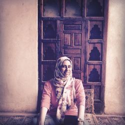 Smiling woman sitting by old closed door