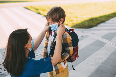 Mom puts a child a mask and escorts to school or kindergarten. 