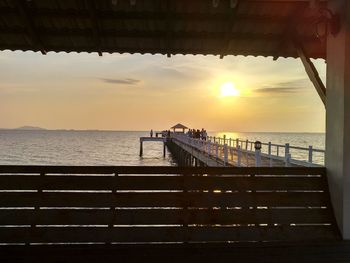 People on pier over sea against sky during sunset