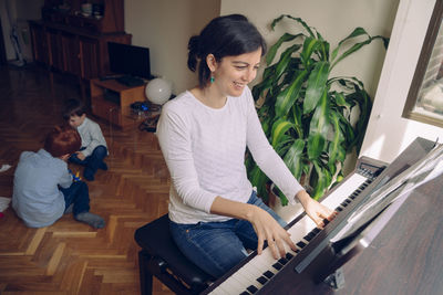 Smiling mother playing piano with siblings enjoying on floor at home