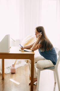 A young attractive student talks on a smartphone while studying at home, discusses homework 