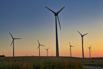 Windmills on field against sky during sunset