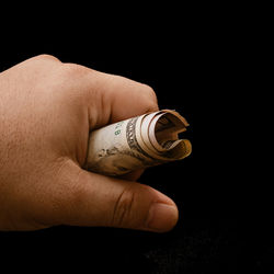 Close-up of hand holding paper currency against black background