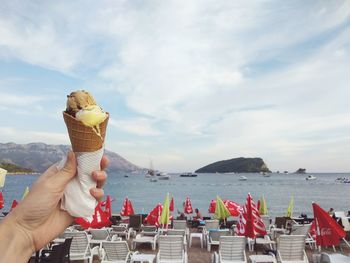 Hand holding ice cream against sea against sky on beach