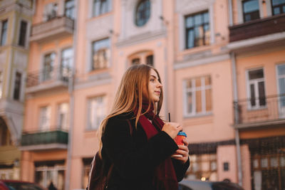 Young thoughtful woman with coffee cup walking on city street