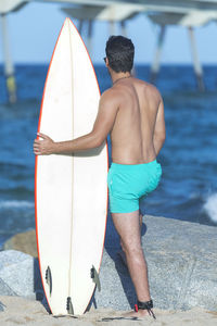 Rear view of shirtless man with surfboard