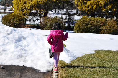 Rear view of girl walking by plants during winter