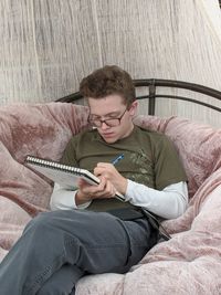 Teenage boy drawing on a sketch pad while sitting in a large chair