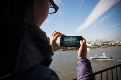Woman photographing sea through mobile phone against sky